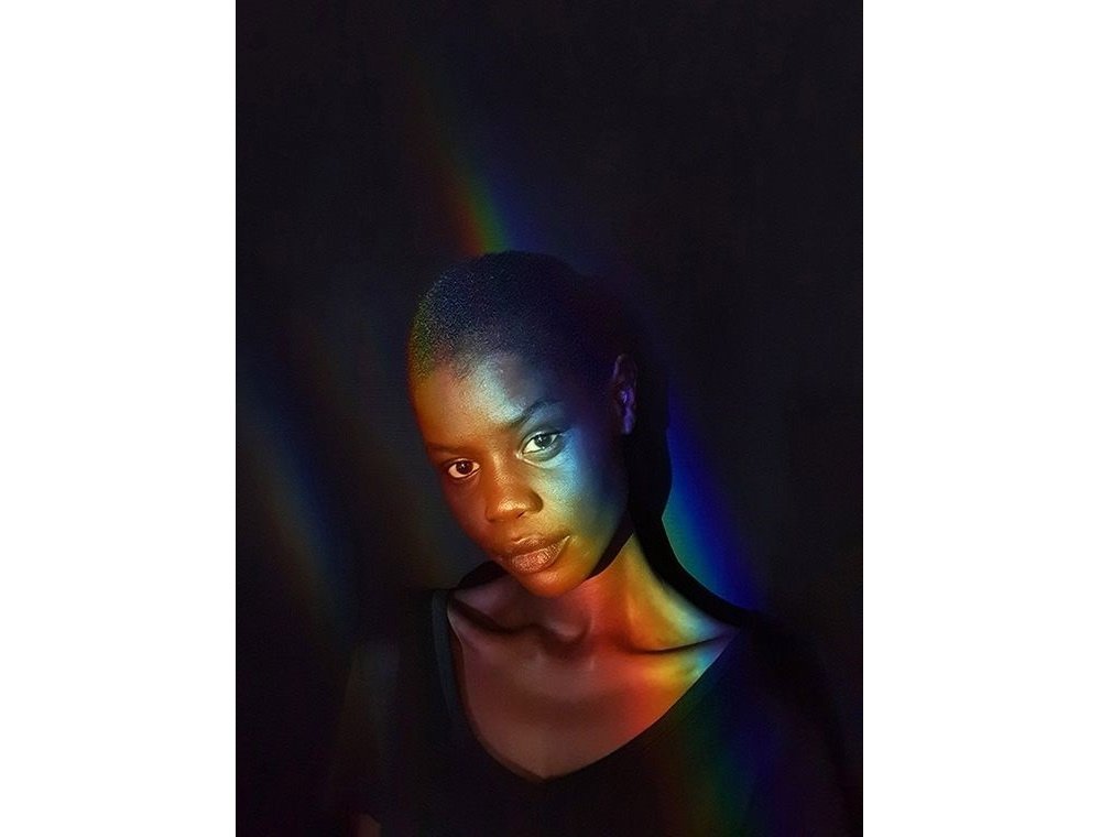 Selfie captured by Galaxy S10 plus of a woman in a low-light space with a rainbow light glowing across her face.