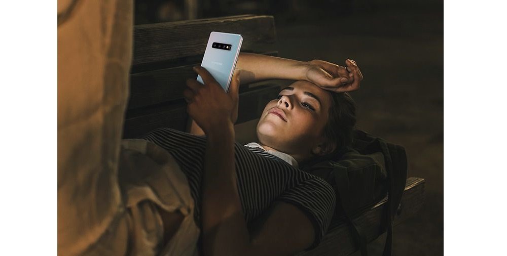 Image of a woman laying on a bench at night using the Galaxy S10 plus.