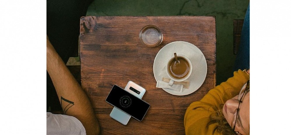 Image of a man and woman at a cafe with a coffee on the table and two Galaxy S10 plus phones, with one powersharing with the other.