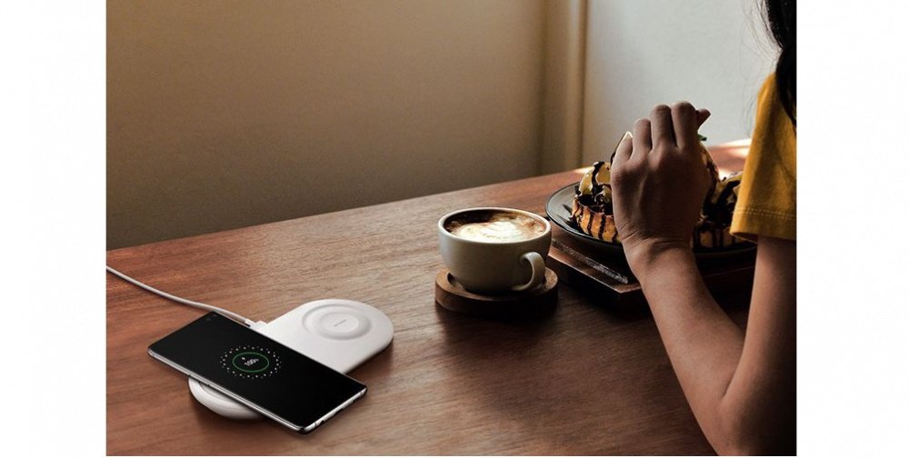Image of a person sitting at a table with a coffee cup, eating with their Galaxy S10 plus charging on the Wireless Charger Duo Pad.
